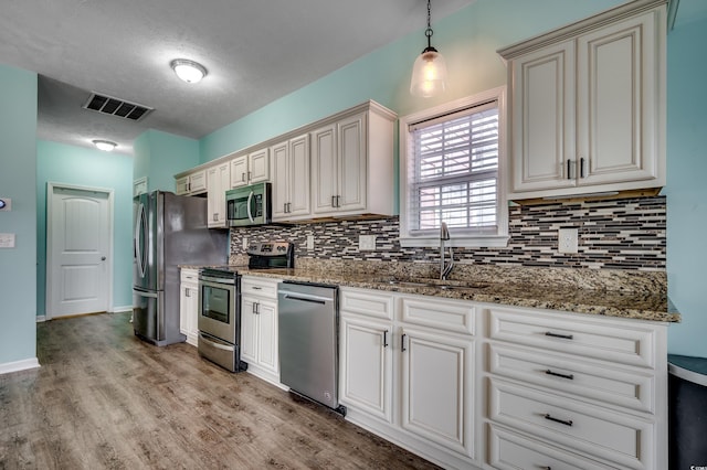 kitchen with light hardwood / wood-style flooring, backsplash, hanging light fixtures, sink, and stainless steel appliances