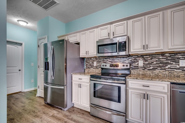 kitchen featuring light wood-type flooring, light stone counters, tasteful backsplash, and stainless steel appliances