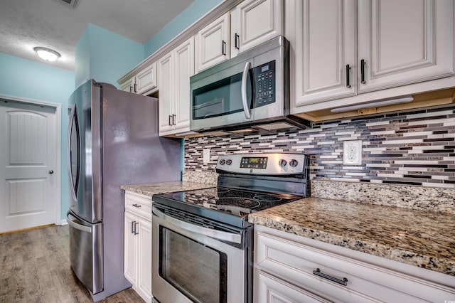 kitchen featuring appliances with stainless steel finishes, backsplash, white cabinetry, light wood-type flooring, and light stone countertops