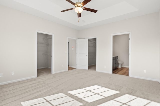 unfurnished bedroom featuring light carpet, ensuite bathroom, ceiling fan, a spacious closet, and a closet