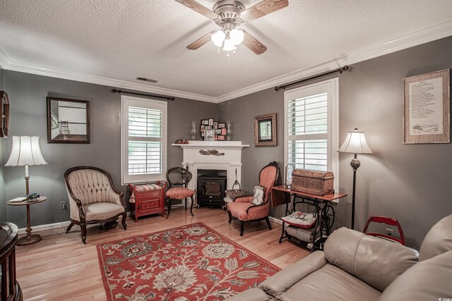 sitting room with a textured ceiling, light wood-type flooring, ornamental molding, and ceiling fan