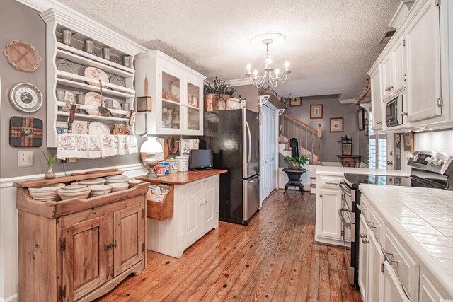 kitchen with light wood-type flooring, appliances with stainless steel finishes, hanging light fixtures, and white cabinets