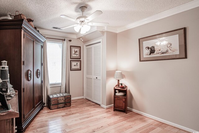 living area featuring a textured ceiling, light wood-type flooring, ornamental molding, and ceiling fan