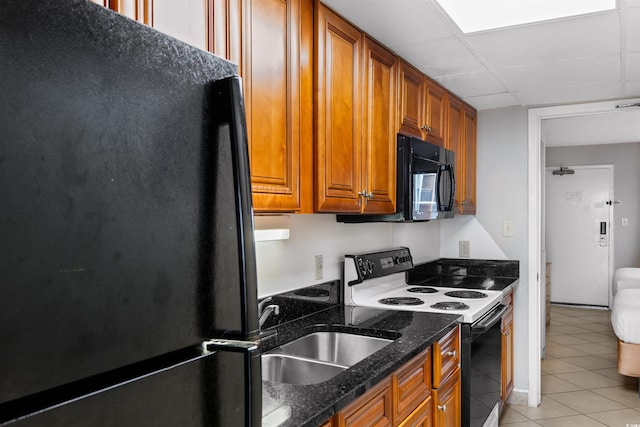 kitchen featuring light tile patterned floors, sink, black appliances, a drop ceiling, and dark stone counters