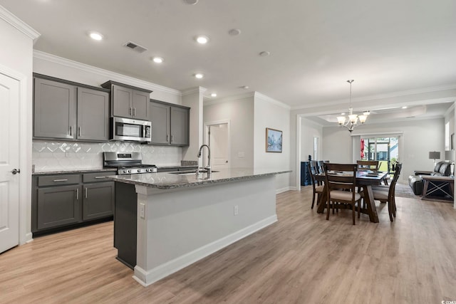 kitchen featuring backsplash, stainless steel appliances, light hardwood / wood-style floors, a center island with sink, and gray cabinets