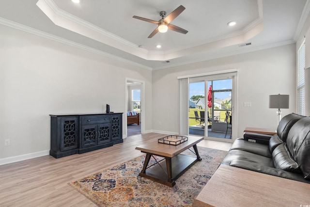 living room with ceiling fan, light wood-type flooring, crown molding, and a tray ceiling