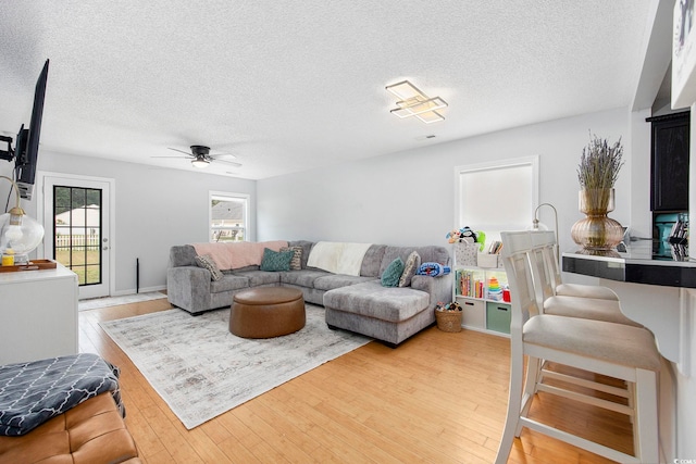 living room with ceiling fan, a textured ceiling, and light hardwood / wood-style flooring