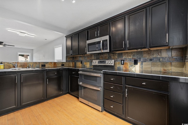 kitchen featuring dark countertops, light wood-style flooring, appliances with stainless steel finishes, and a sink