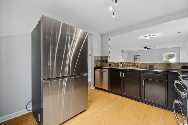 kitchen featuring dark brown cabinetry, dark countertops, stainless steel appliances, light wood-style floors, and a sink