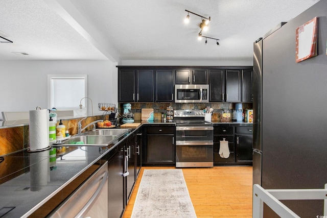 kitchen with backsplash, appliances with stainless steel finishes, a textured ceiling, light hardwood / wood-style flooring, and sink