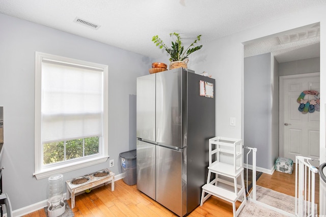 kitchen with a textured ceiling, light wood-type flooring, and stainless steel fridge