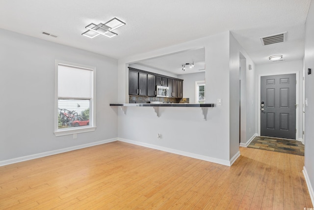 kitchen with tasteful backsplash, visible vents, light wood-style flooring, stainless steel microwave, and a breakfast bar area