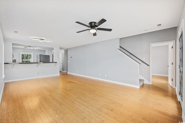 unfurnished living room featuring light wood finished floors, visible vents, a ceiling fan, baseboards, and stairs