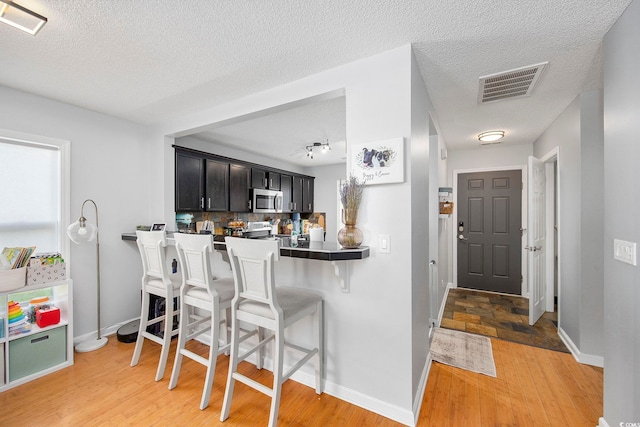 kitchen with a kitchen breakfast bar, kitchen peninsula, stainless steel appliances, a textured ceiling, and light hardwood / wood-style floors