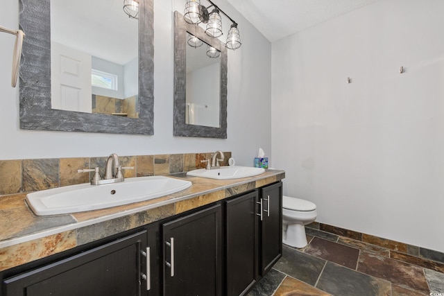 full bathroom featuring toilet, stone tile floors, double vanity, and a sink