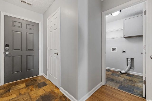 foyer entrance with stone tile floors, a textured ceiling, visible vents, and baseboards