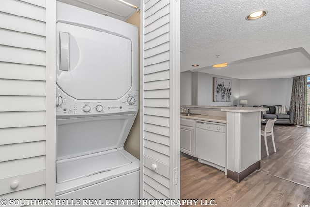 laundry room with sink, a textured ceiling, dark hardwood / wood-style floors, and stacked washing maching and dryer