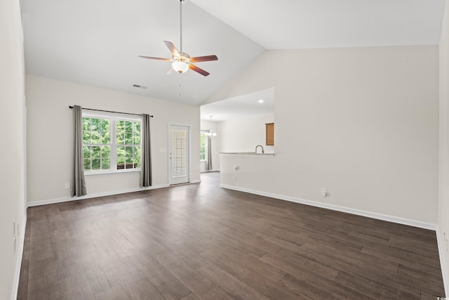 unfurnished living room with ceiling fan with notable chandelier, high vaulted ceiling, and dark wood-type flooring