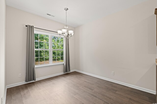 spare room with hardwood / wood-style flooring and a notable chandelier