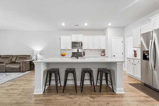 kitchen with an island with sink, a kitchen bar, light hardwood / wood-style floors, sink, and stainless steel appliances