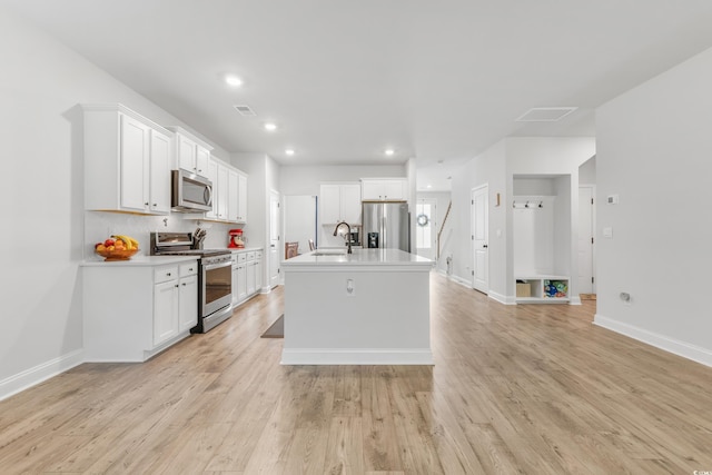 kitchen with stainless steel appliances, a kitchen island with sink, white cabinets, and light hardwood / wood-style flooring