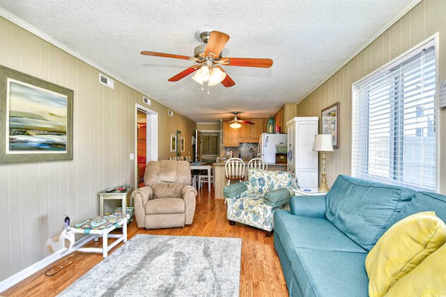 living room with a textured ceiling, light hardwood / wood-style floors, wood walls, crown molding, and ceiling fan