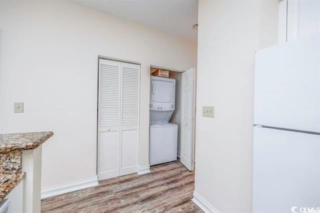 kitchen featuring stacked washer / drying machine, stone counters, white fridge, and light wood-type flooring