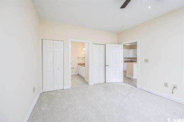 unfurnished bedroom featuring ceiling fan, light carpet, connected bathroom, and two closets