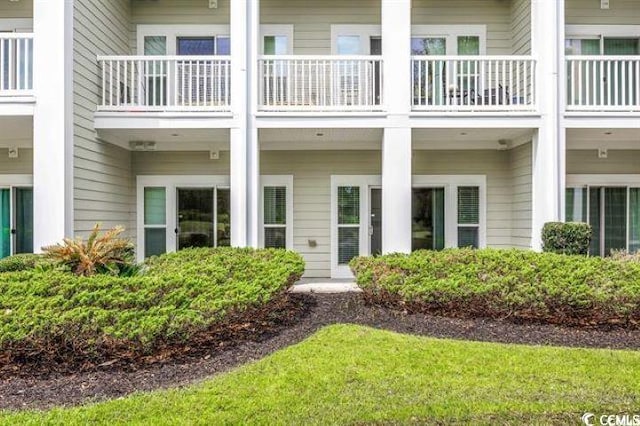 view of exterior entry with a balcony and a lawn