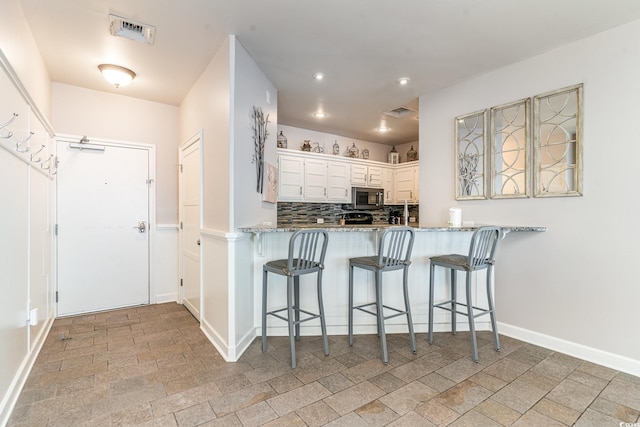 kitchen with a peninsula, a kitchen bar, stainless steel microwave, and white cabinets