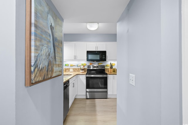 kitchen with appliances with stainless steel finishes, light wood-type flooring, white cabinetry, and sink