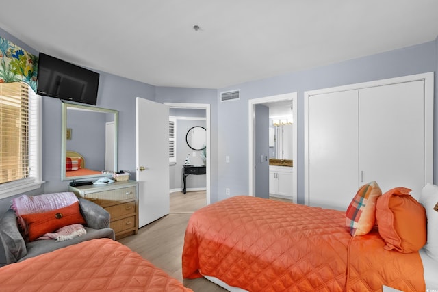 bedroom with light hardwood / wood-style floors, ensuite bath, and a closet