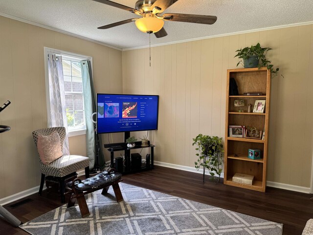 sitting room featuring wooden walls, ornamental molding, dark wood-type flooring, and ceiling fan