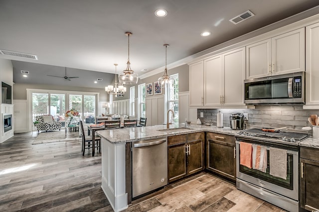 kitchen with light stone counters, white cabinetry, ceiling fan with notable chandelier, appliances with stainless steel finishes, and sink