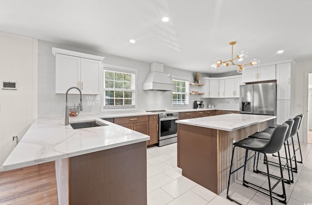 kitchen with stainless steel appliances, white cabinets, a center island, and premium range hood