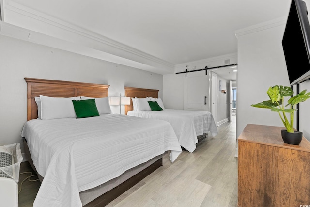 bedroom featuring light hardwood / wood-style flooring, crown molding, and a barn door