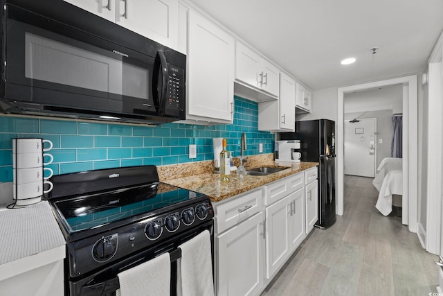 kitchen featuring decorative backsplash, white cabinets, black appliances, light hardwood / wood-style flooring, and sink