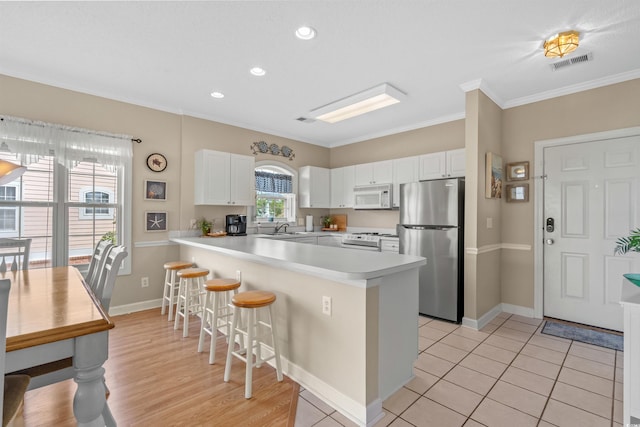 kitchen with stainless steel refrigerator, white cabinetry, light tile patterned floors, kitchen peninsula, and crown molding