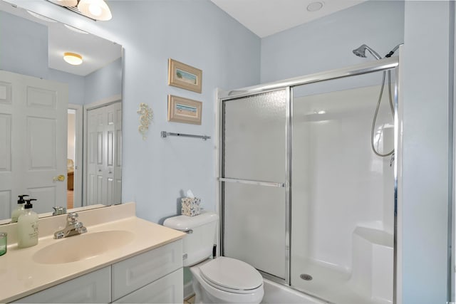 bathroom featuring a shower with door, vanity, and toilet