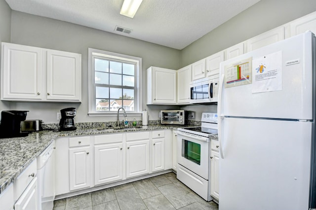 kitchen featuring sink, white cabinetry, light stone countertops, white appliances, and light tile patterned floors