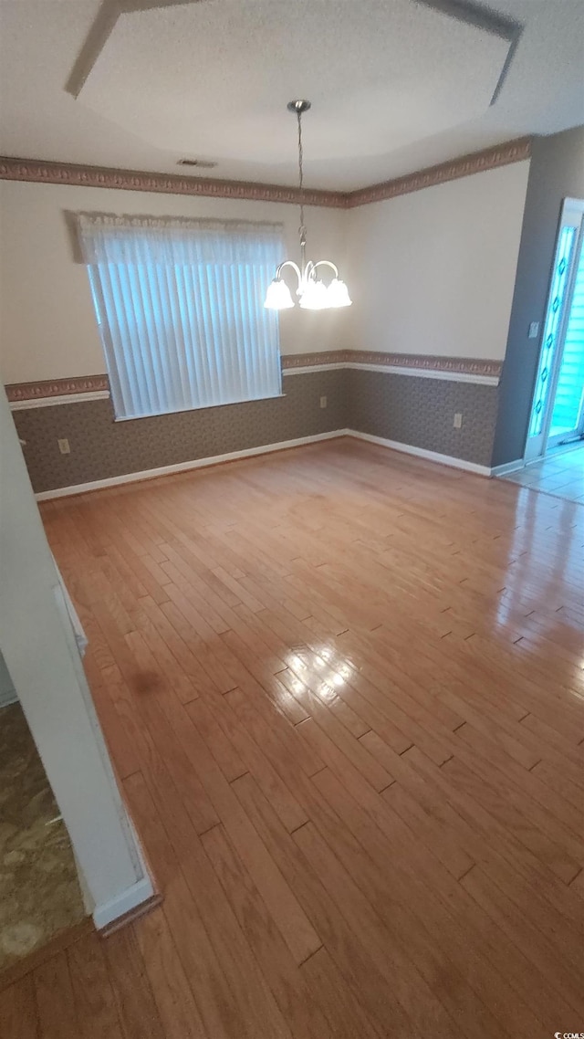 unfurnished dining area with a wainscoted wall, wallpapered walls, wood finished floors, and an inviting chandelier