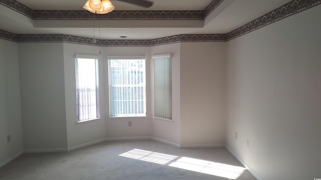 spare room featuring a wealth of natural light, carpet, a raised ceiling, and baseboards