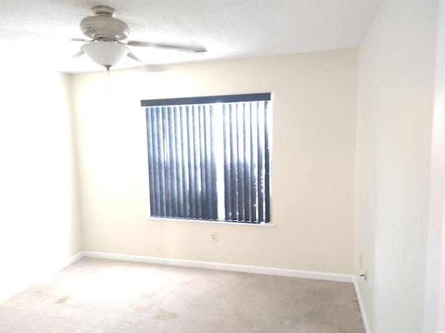 spare room featuring light carpet, ceiling fan, a textured ceiling, and baseboards