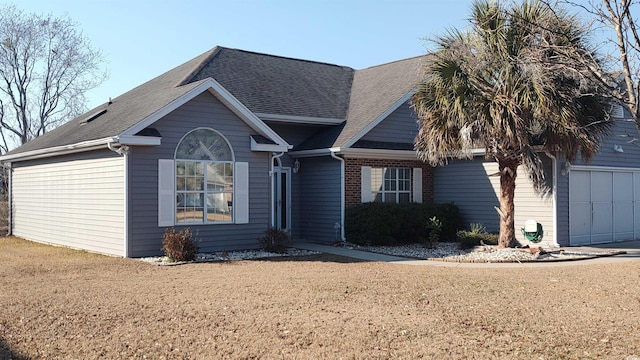 view of front of property featuring a garage, brick siding, roof with shingles, and a front yard