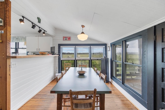 dining space with lofted ceiling, rail lighting, hardwood / wood-style floors, and wood walls