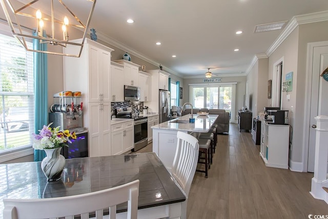 kitchen featuring visible vents, white cabinets, appliances with stainless steel finishes, a kitchen bar, and a center island with sink