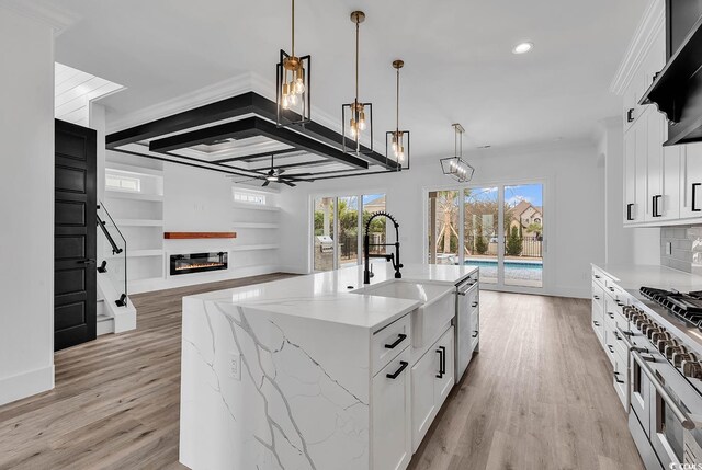 kitchen featuring hanging light fixtures, ceiling fan, light stone countertops, a kitchen island with sink, and white cabinets