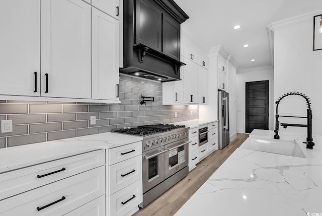 kitchen with white cabinetry, high quality appliances, light stone countertops, and sink