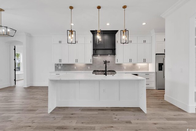 kitchen with pendant lighting, white cabinets, stainless steel fridge, light stone counters, and a spacious island