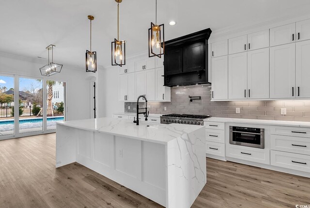 kitchen featuring stainless steel appliances, ornamental molding, hanging light fixtures, and a center island with sink